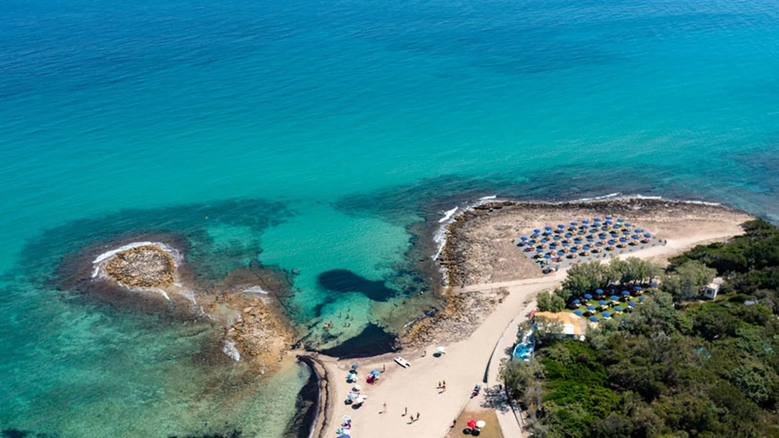 La spiaggia di Pilone con acqua turchese, scogli affioranti e ombrelloni